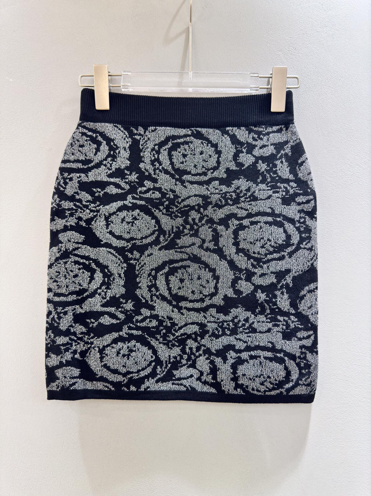 A navy blue mini skirt with a gray and white floral pattern, hanging on a clear plastic hanger with two wooden clips against a plain off-white wall.