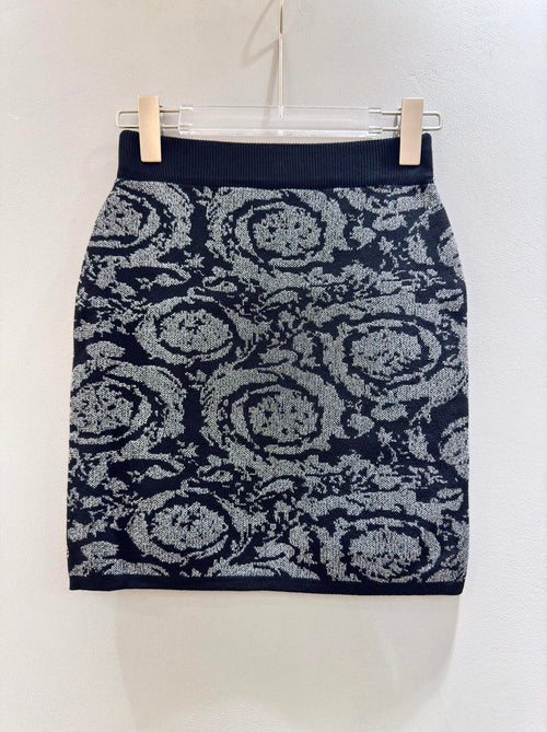 A navy blue mini skirt with a gray and white floral pattern, hanging on a clear plastic hanger with two wooden clips against a plain off-white wall.